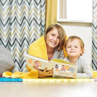 Two siblings happily looking through a personalised photobook, showcasing special moments. Take advantage of RapidStudio’s discounted photobook offers to preserve your precious memories.